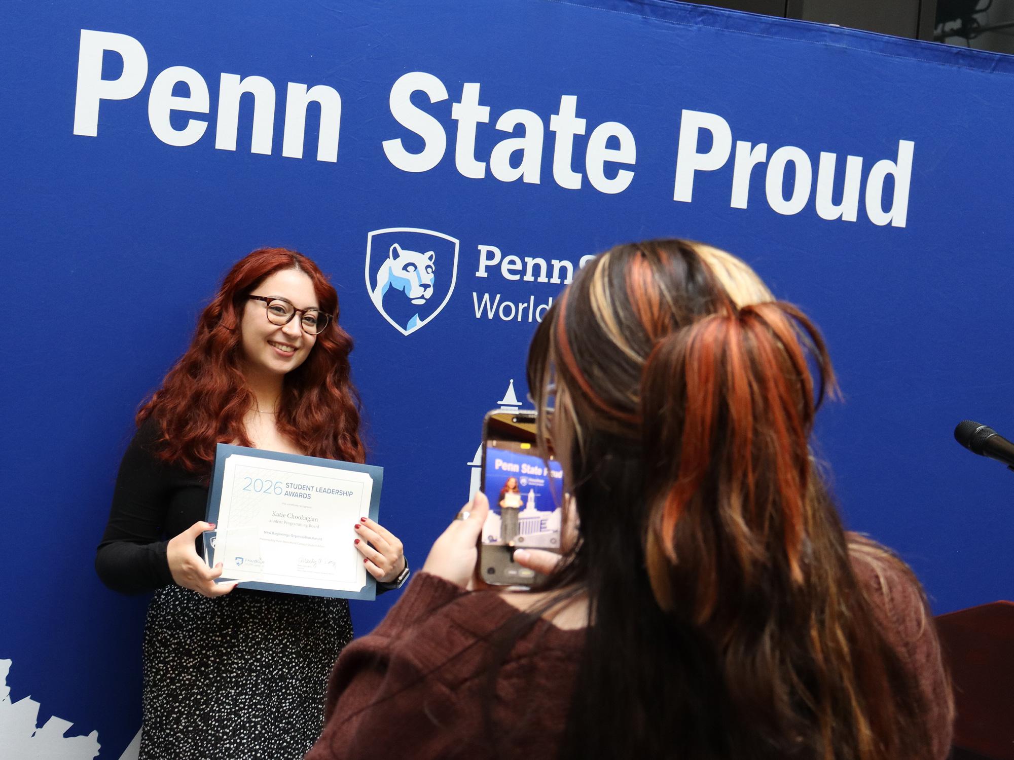 A woman takes a photo of another woman who is holding a certificate.