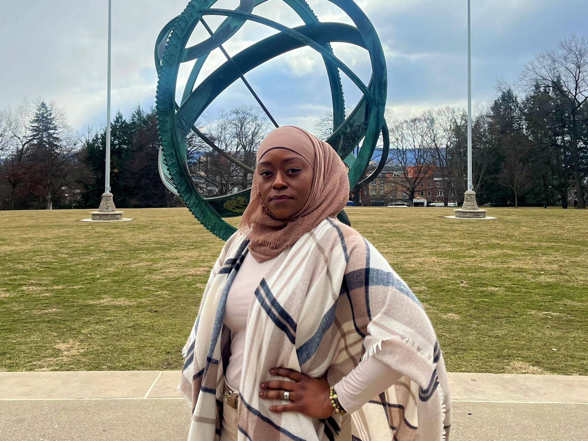 A woman stands in front of a sculpture on a green lawn.