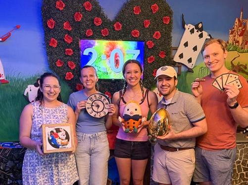 Sonia Lloyd and four other team members pose together in front of the Alice in Wonderland-themed escape room. 