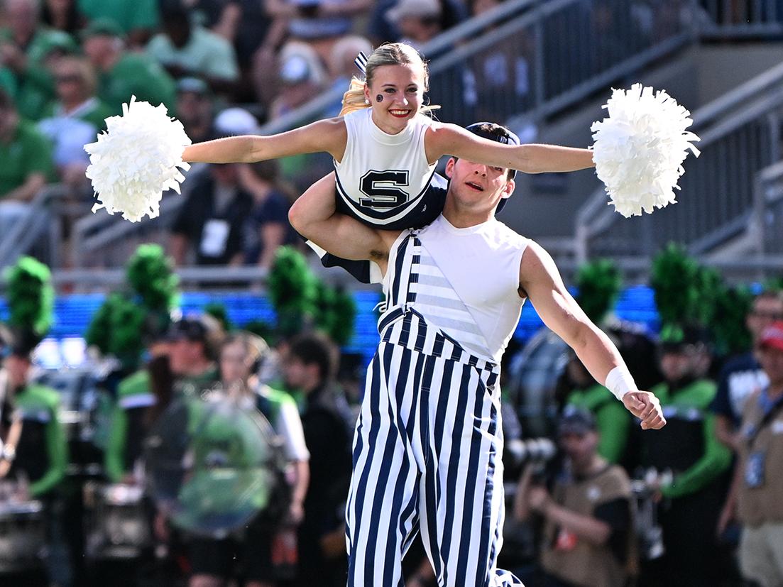 Female cheerleader balances on male cheerleader's shoulder