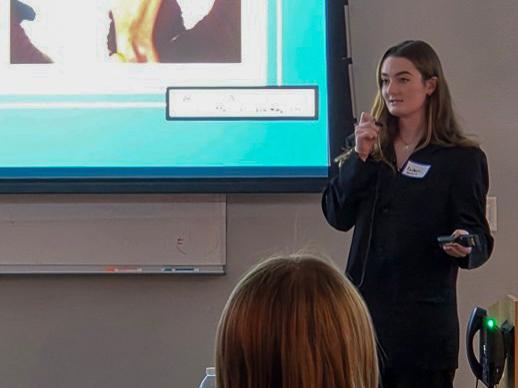 Colleen McKenzie holds a tiny microphone while presenting at the front of the room.
