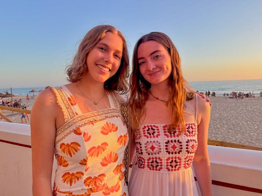 McKenzie and Estes stand together in front of a beach in Cádiz, Spain, at sunset.