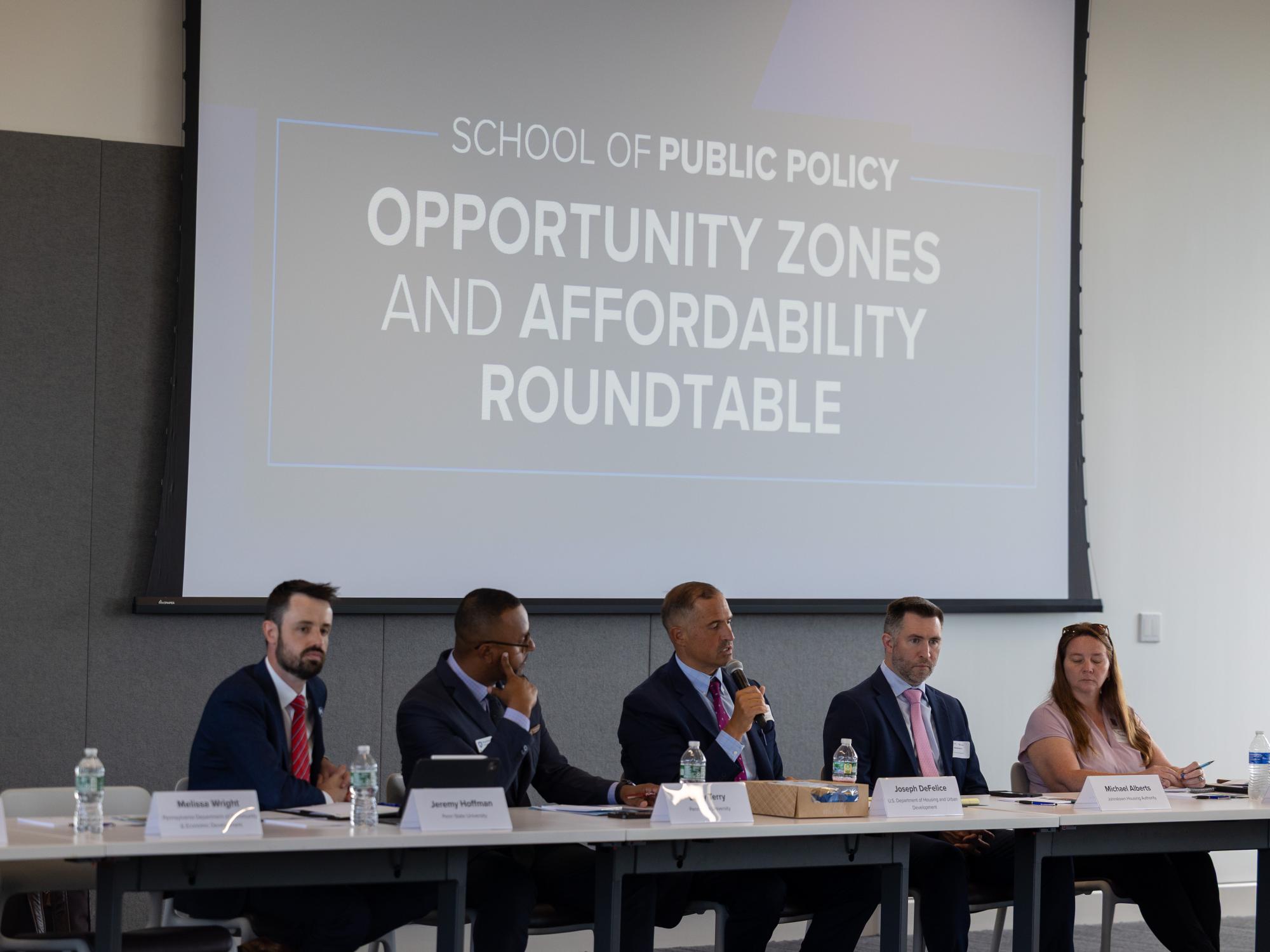 Five people in business attire seated during a meeting led by Joseph DeFelice, holding a microphone.