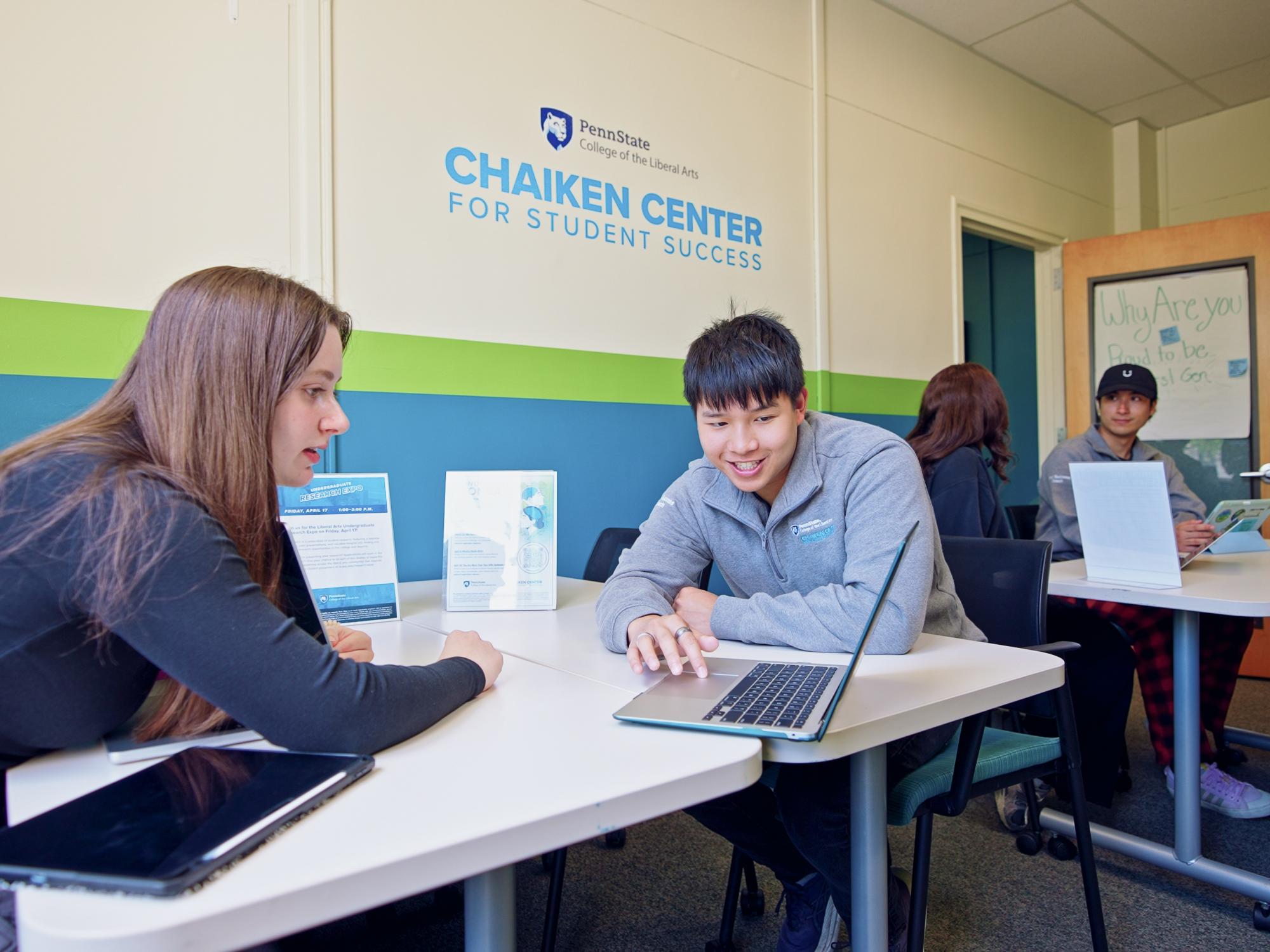 Justin Lai sits at a table using a laptop while another student sits across from them looking at the screen. The wall behind them reads, “Chaiken Center for Student Success.”
