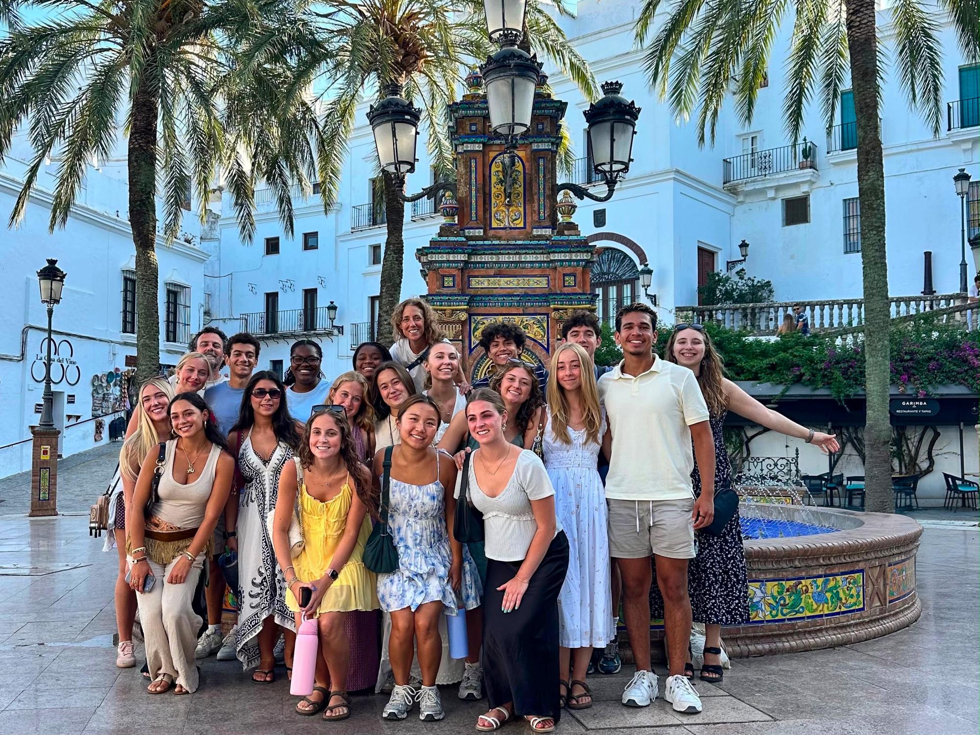 A group of Penn State students visiting in front of a fountain and palm trees.