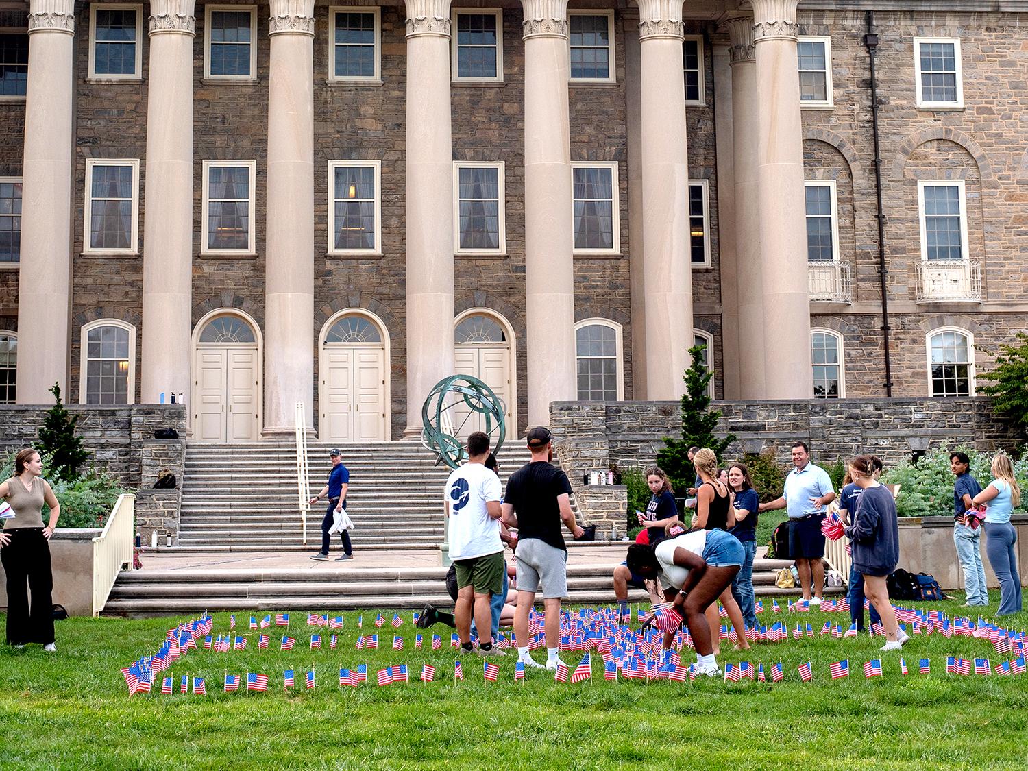 A group of students plant small red, white and blue American flags in the ground in front of Old Main