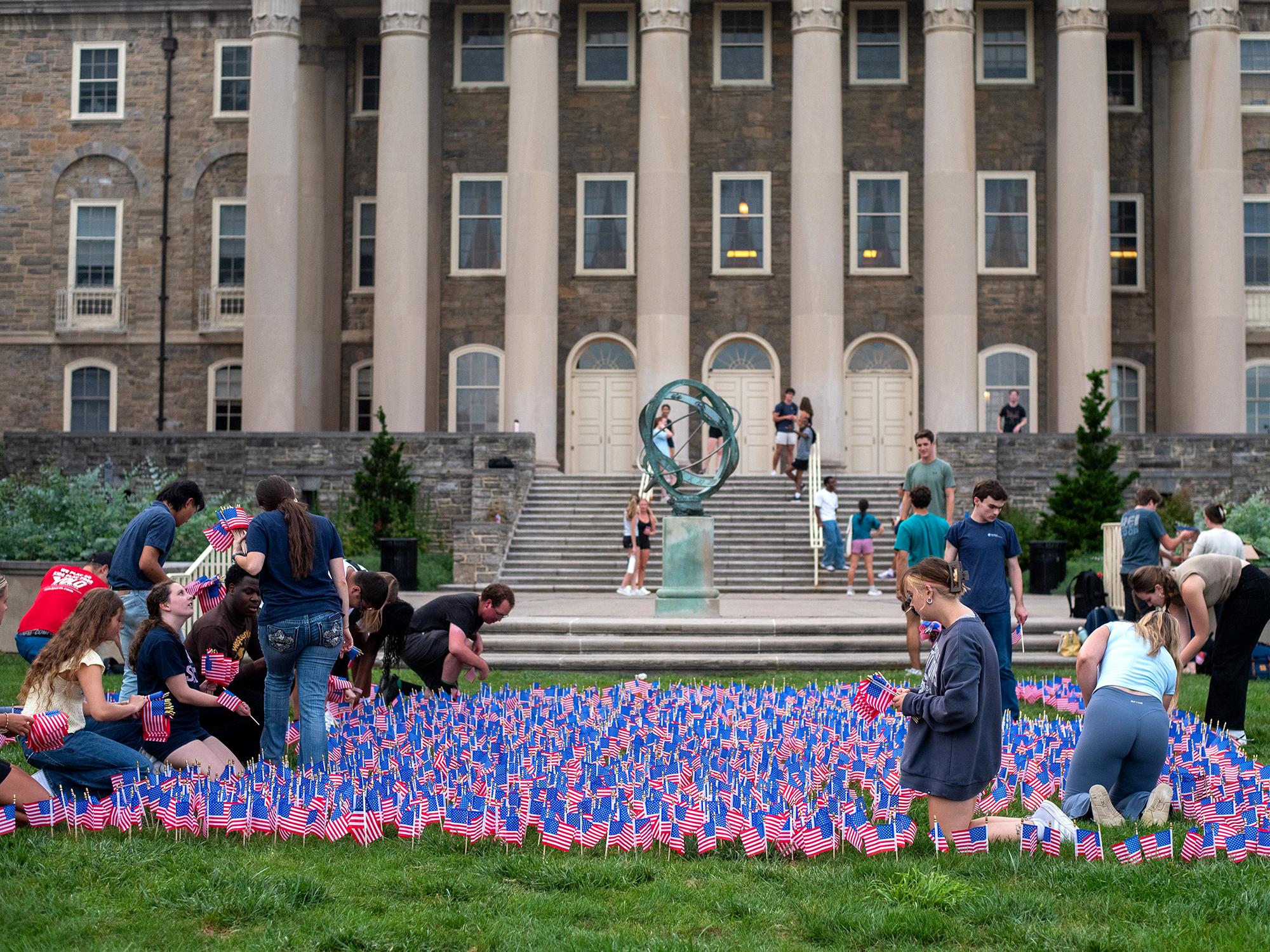 A group of students plant small red, white and blue American flags in the ground in front of Old Main