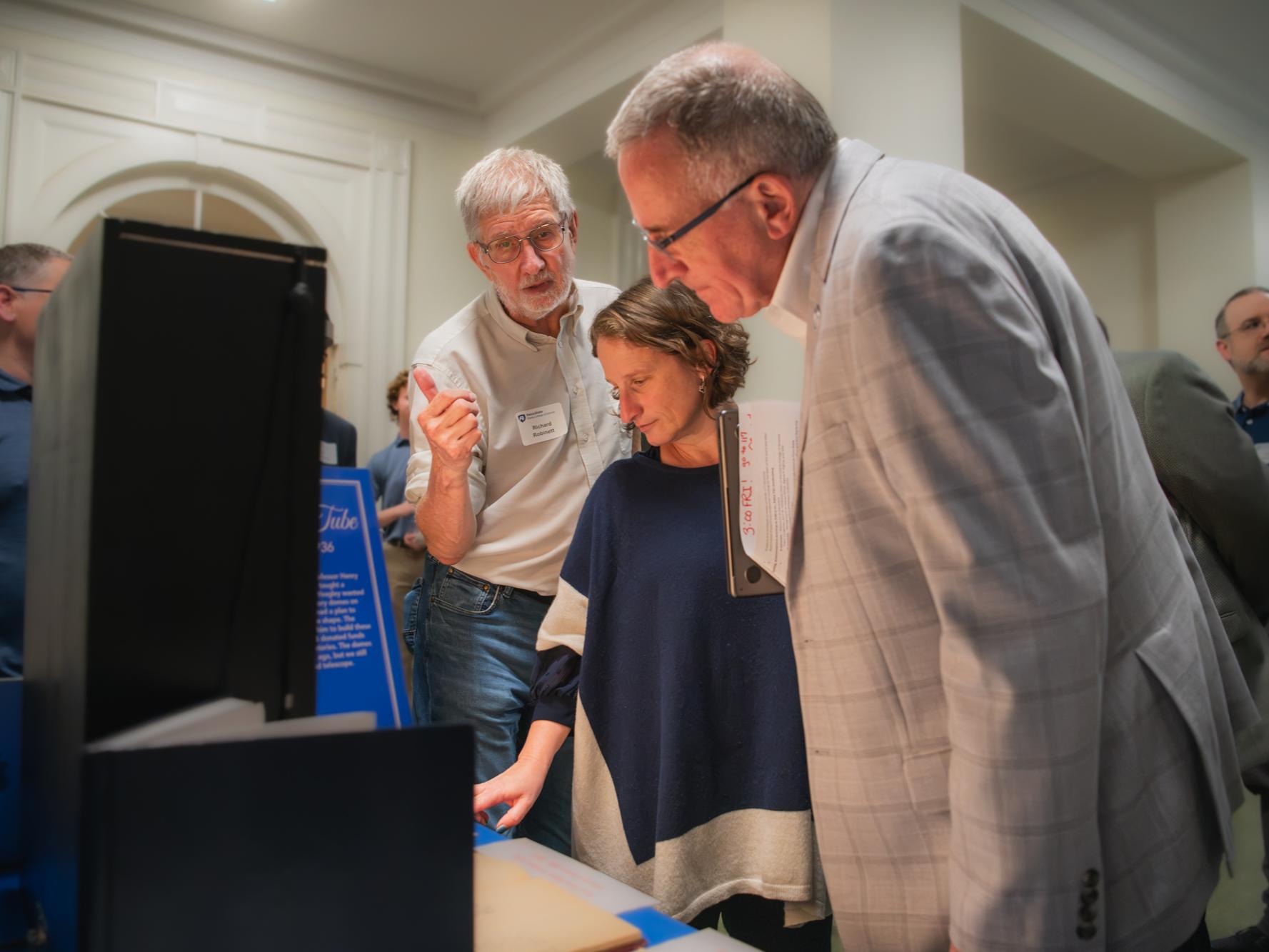Three individuals look at memorabilia on a table