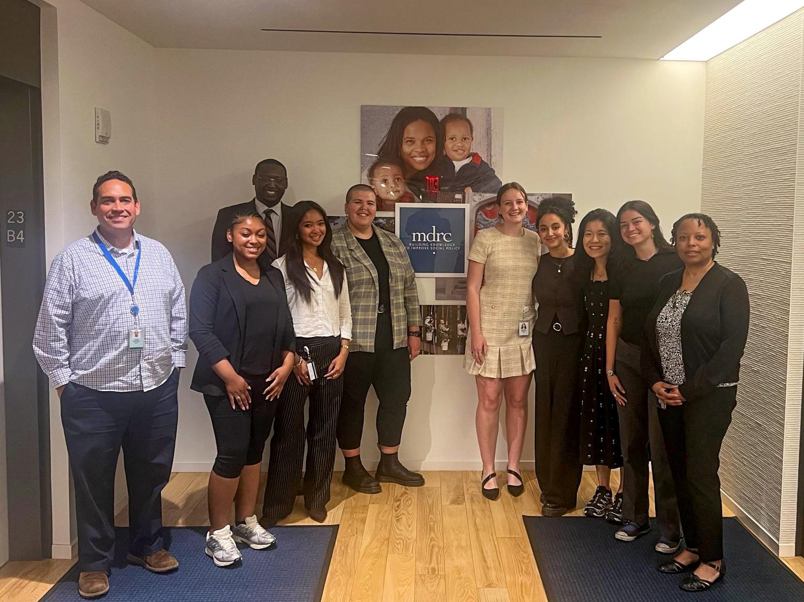 A group of ten diverse professionals, including Madeline Shanafelt, standing in a hallway between two elevators and smiling at the camera.