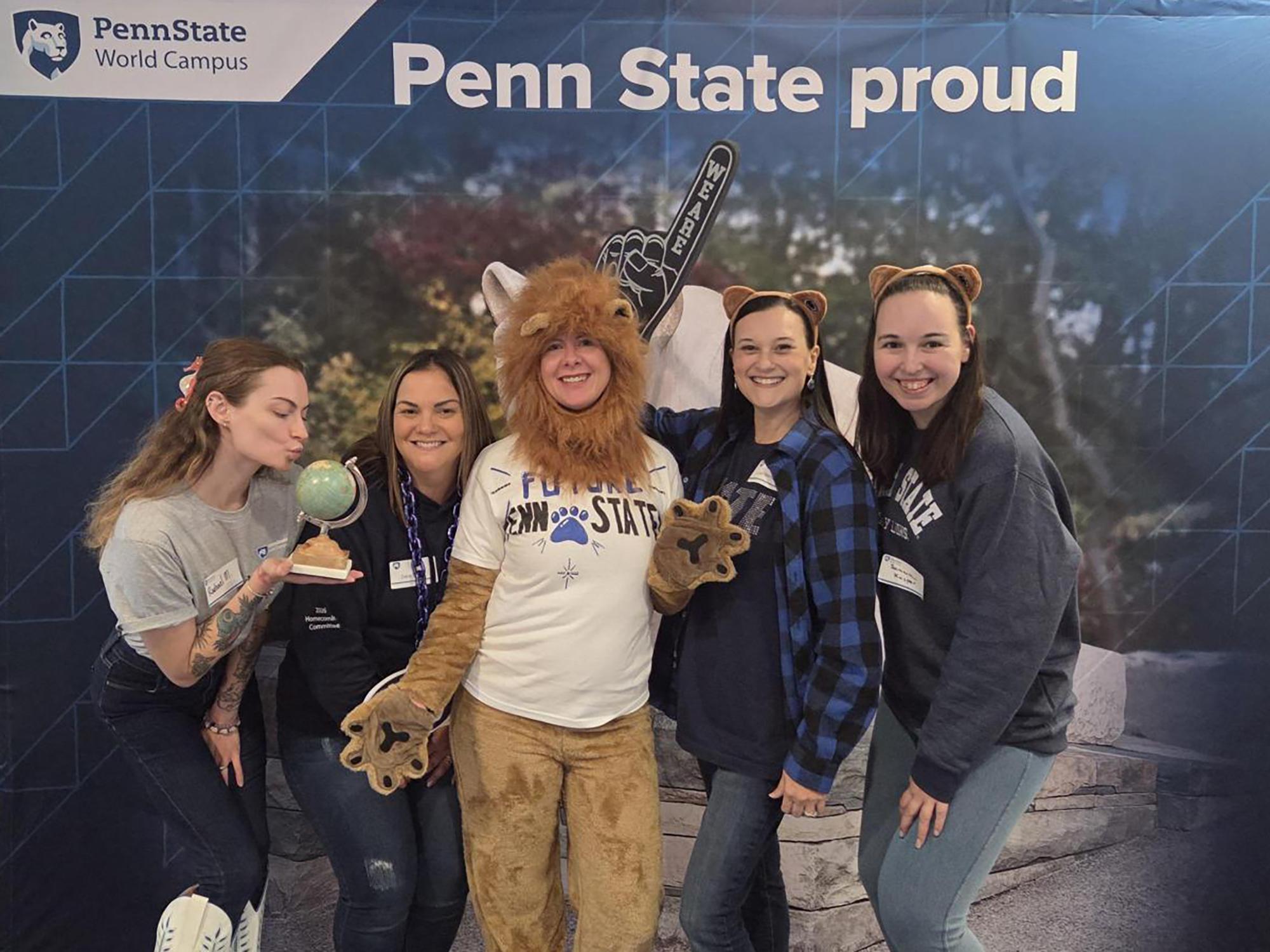 Five people wearing Penn State apparel pose in front of a photo background.