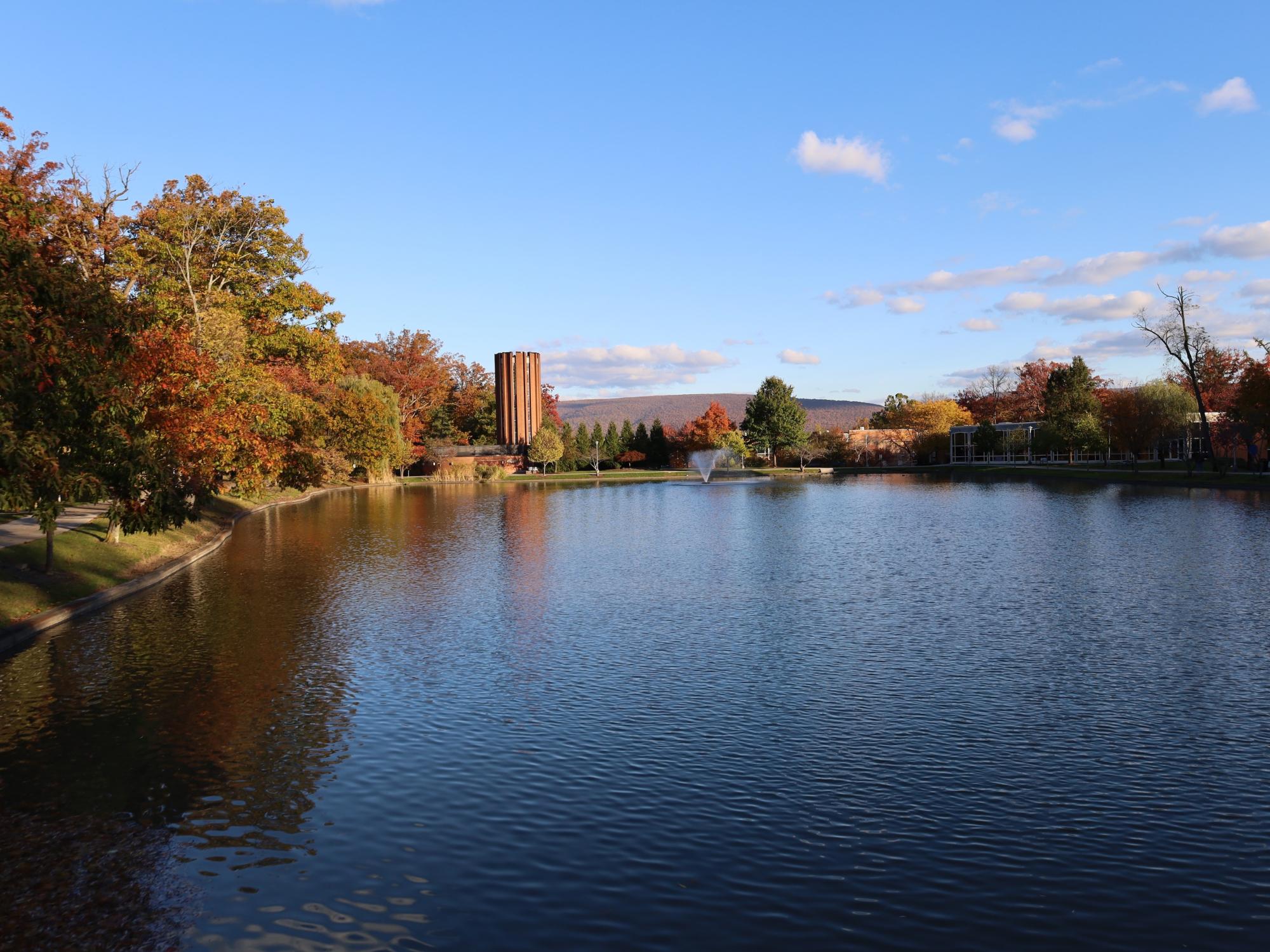 Large reflecting pond surrounded by trees with red and orange foliage.