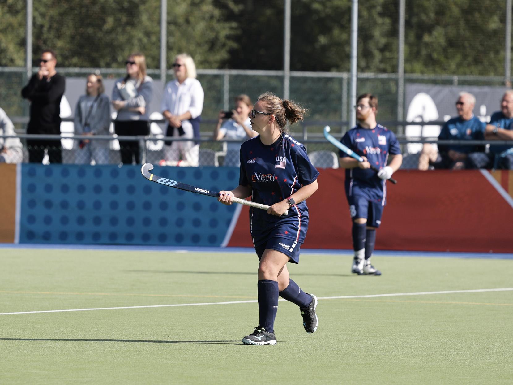 Katie Costello runs, holding a field hockey stick, during a game