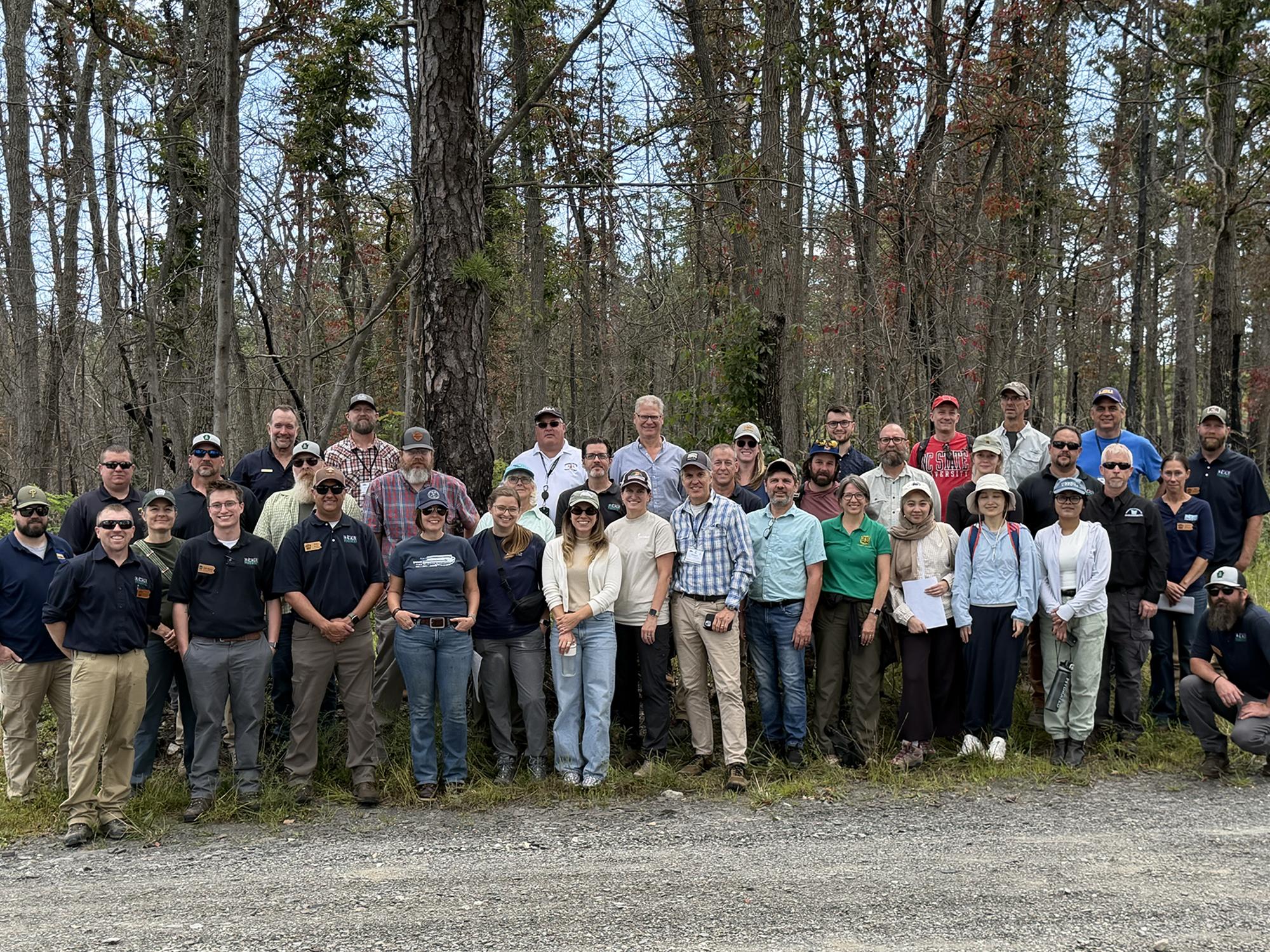 Approximately 40 people wearing outdoor gear and smiling with woody trees in the background