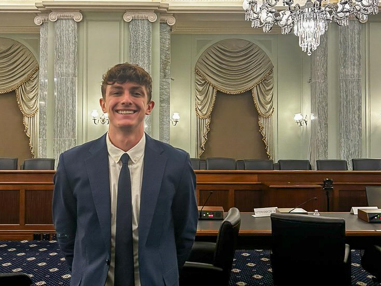 Jansen Hoffard stands smiling in an ornate government hearing chamber.