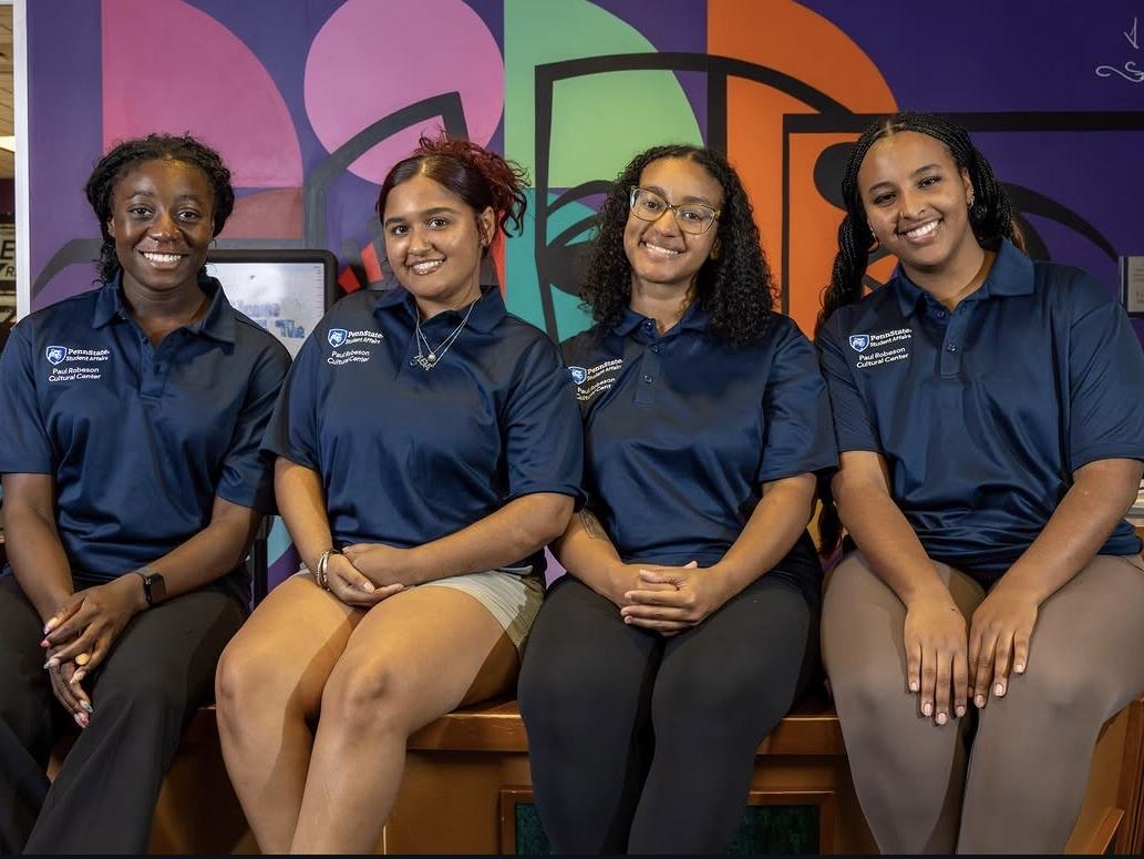 Luna Nunez-Peralta sits with fellow student staff members in front of a colorful mural at the Paul Robeson Cultural Center.