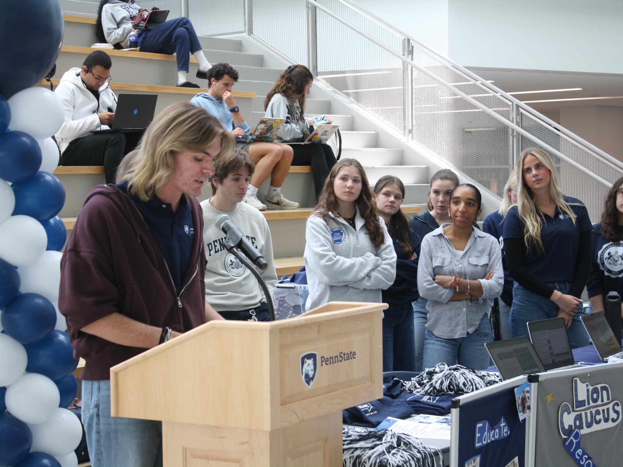 Group of students in Penn State attire listen to speaker at event 