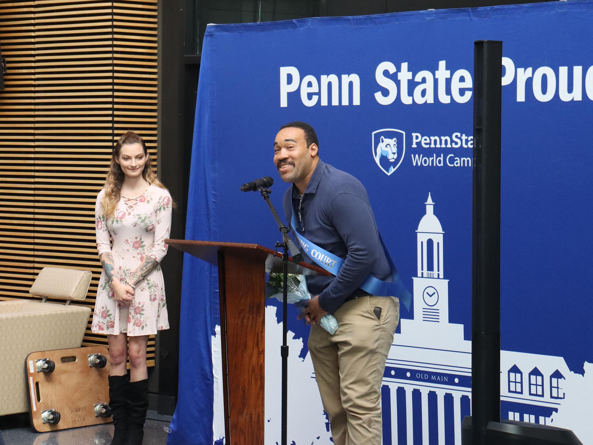 A man speaks at a podium in front of a blue photo background.