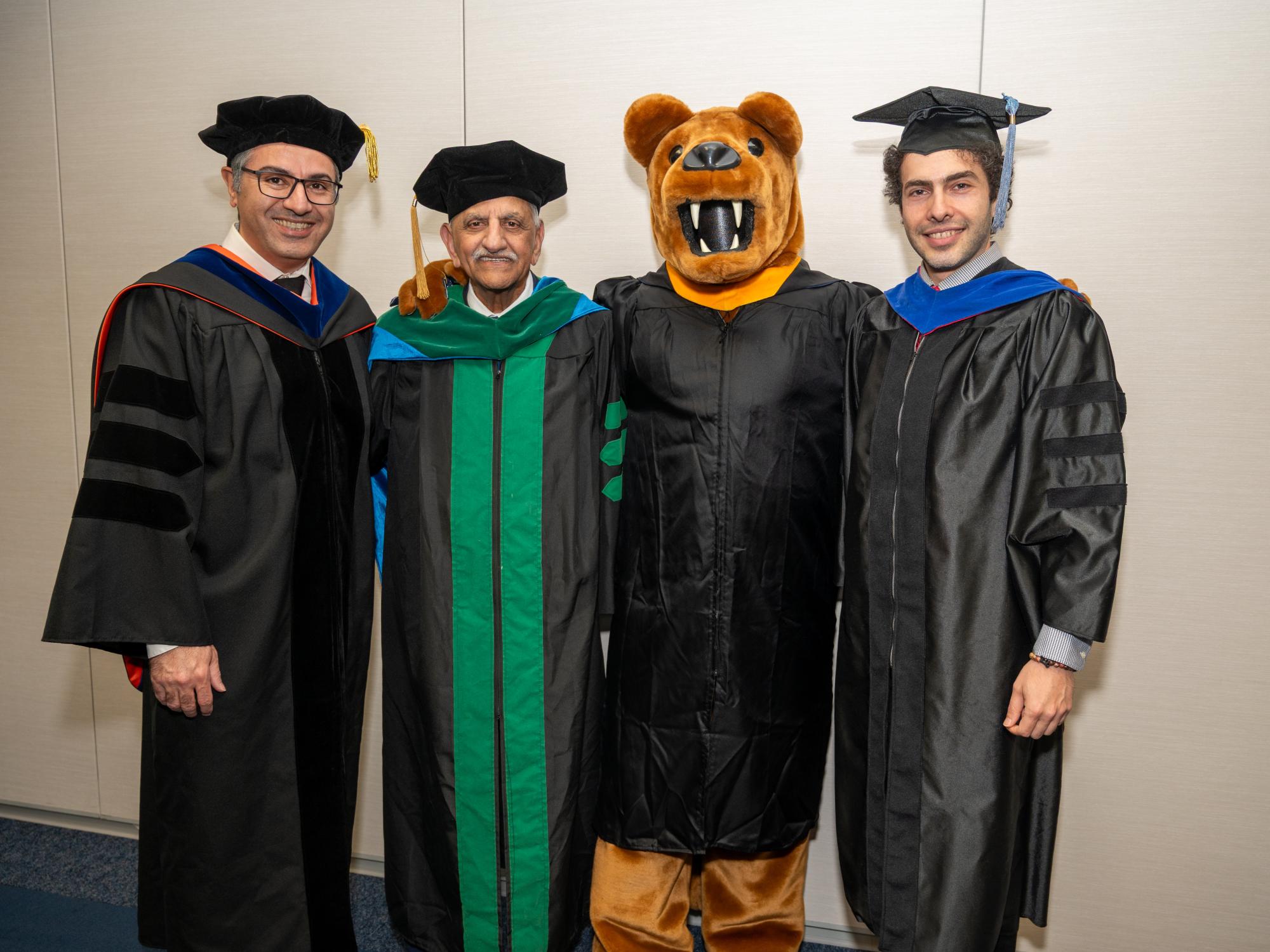 Three men in doctoral academic regalia stand next to the Nittany Lion mascot.