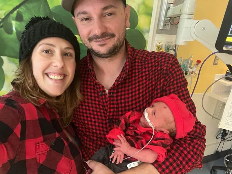 A couple smile as they hold their premature son in the NICU. The baby has a tube taped under his nose.