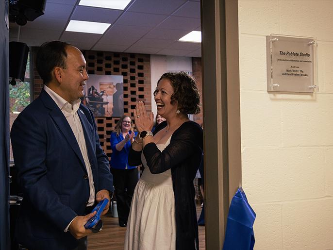 A man and a woman cut a ribbon at the threshold of a large room.