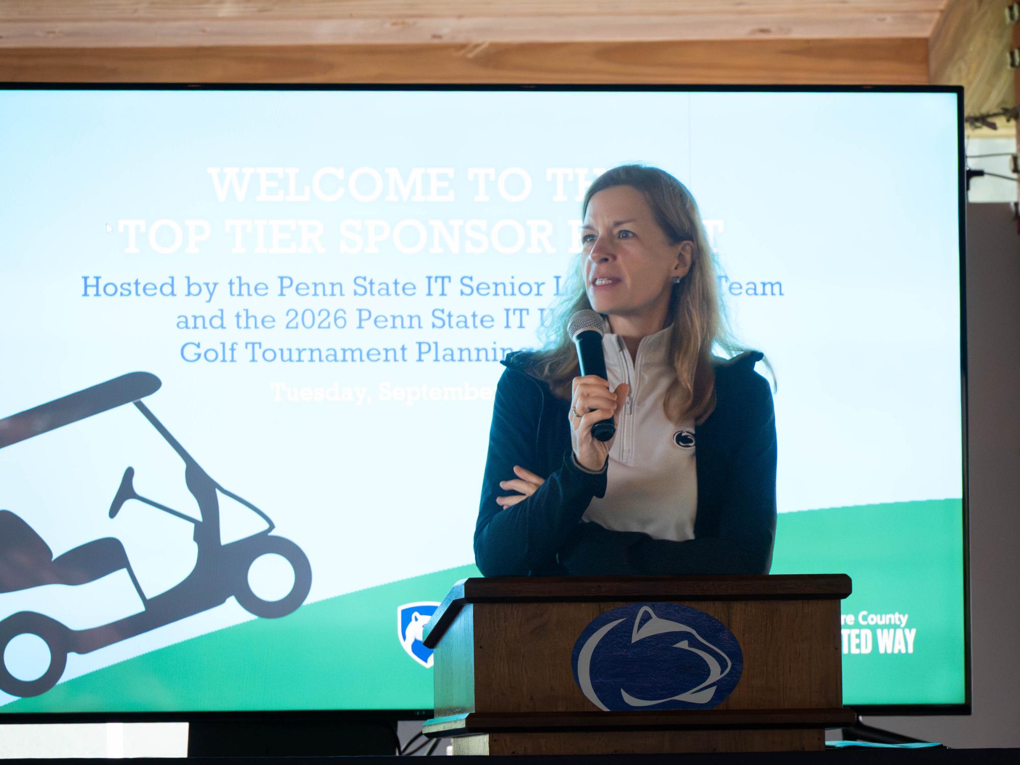 Woman standing at podium in front of background with a golf cart 