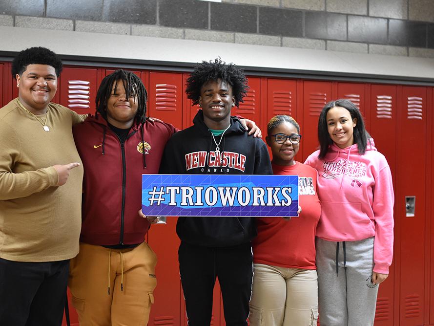 Five students holding a sign that says Trioworks