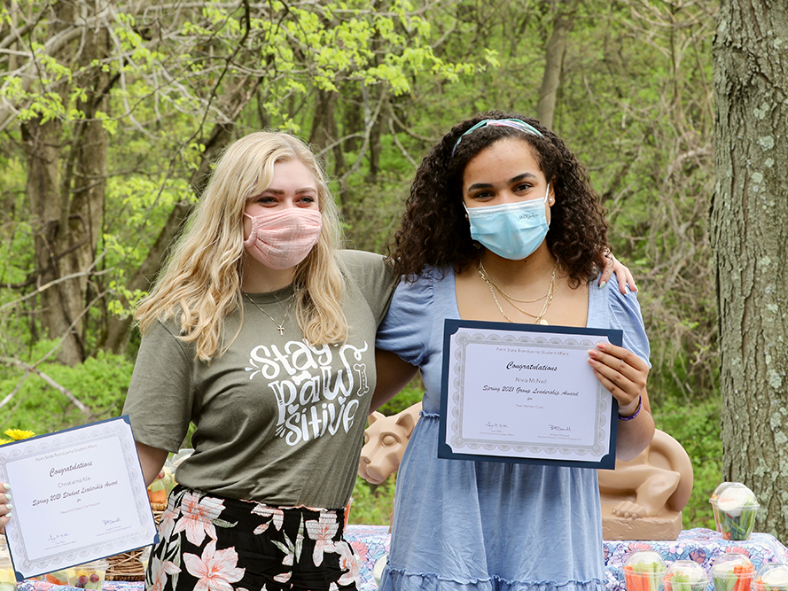 Two female students sharing their award certificates.