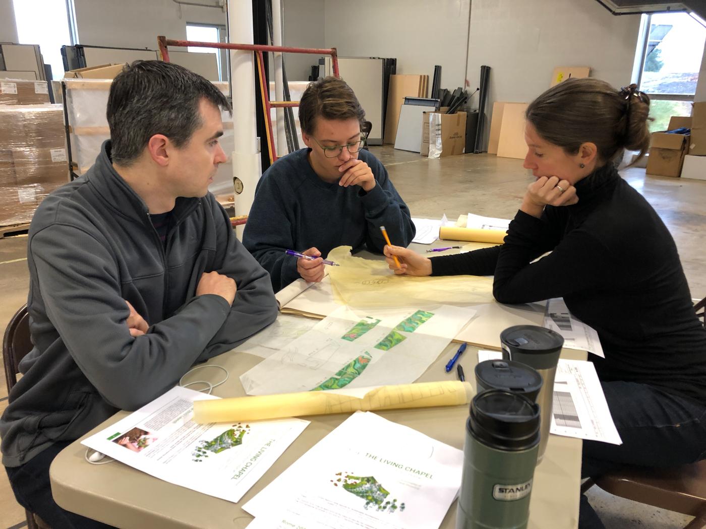 Julian Revie, Becca Newburg and Julian Revie sit around a table with a sketch spread out on the table before them.