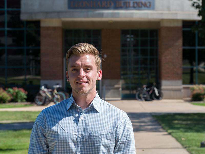 Young man stands in a light-colored shirt for an outdoor photo.