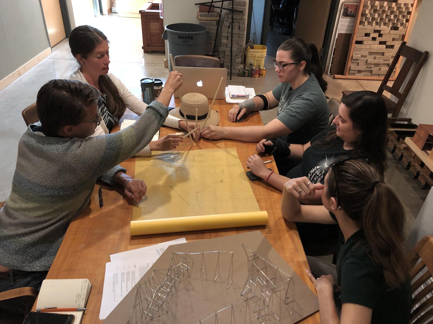 Five members of the design team discuss plans while sitting around a table.