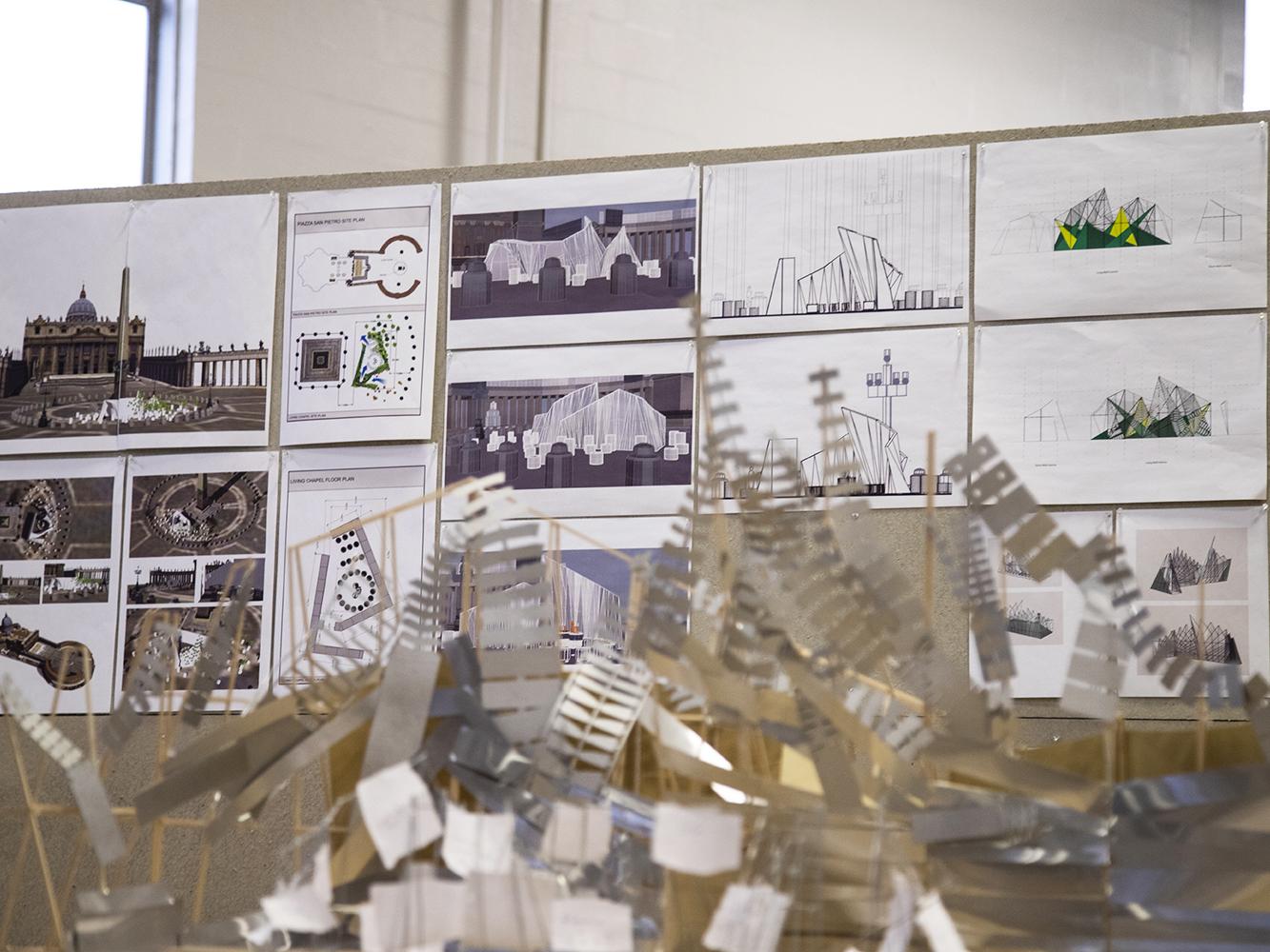 Plans for the Living Chapel are pinned up in the Laundry Building behind an early model that the Penn State team assembled.