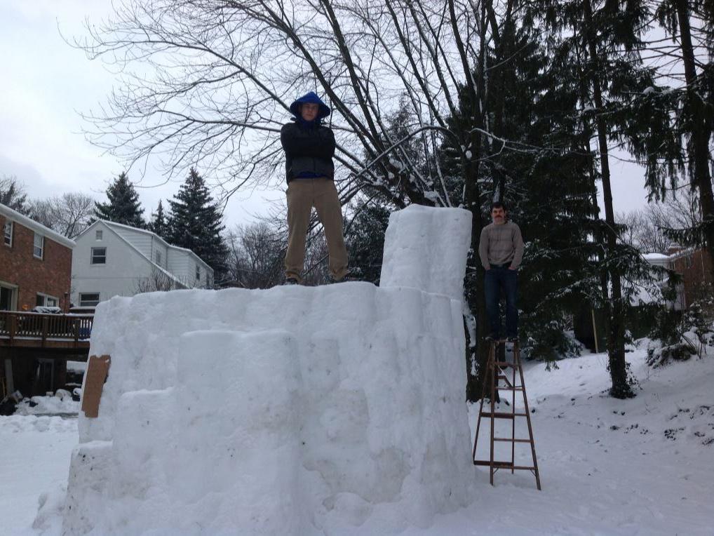 Two males standing on an 11-foot snow fort.