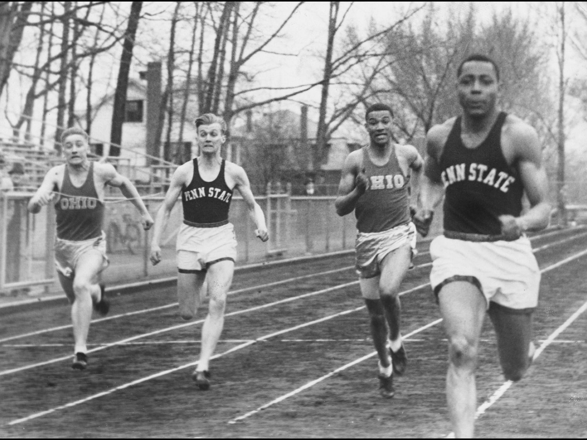 four runners, two wearing Ohio jerseys and two wearing Penn State jerseys, with Penn State runner leading the race