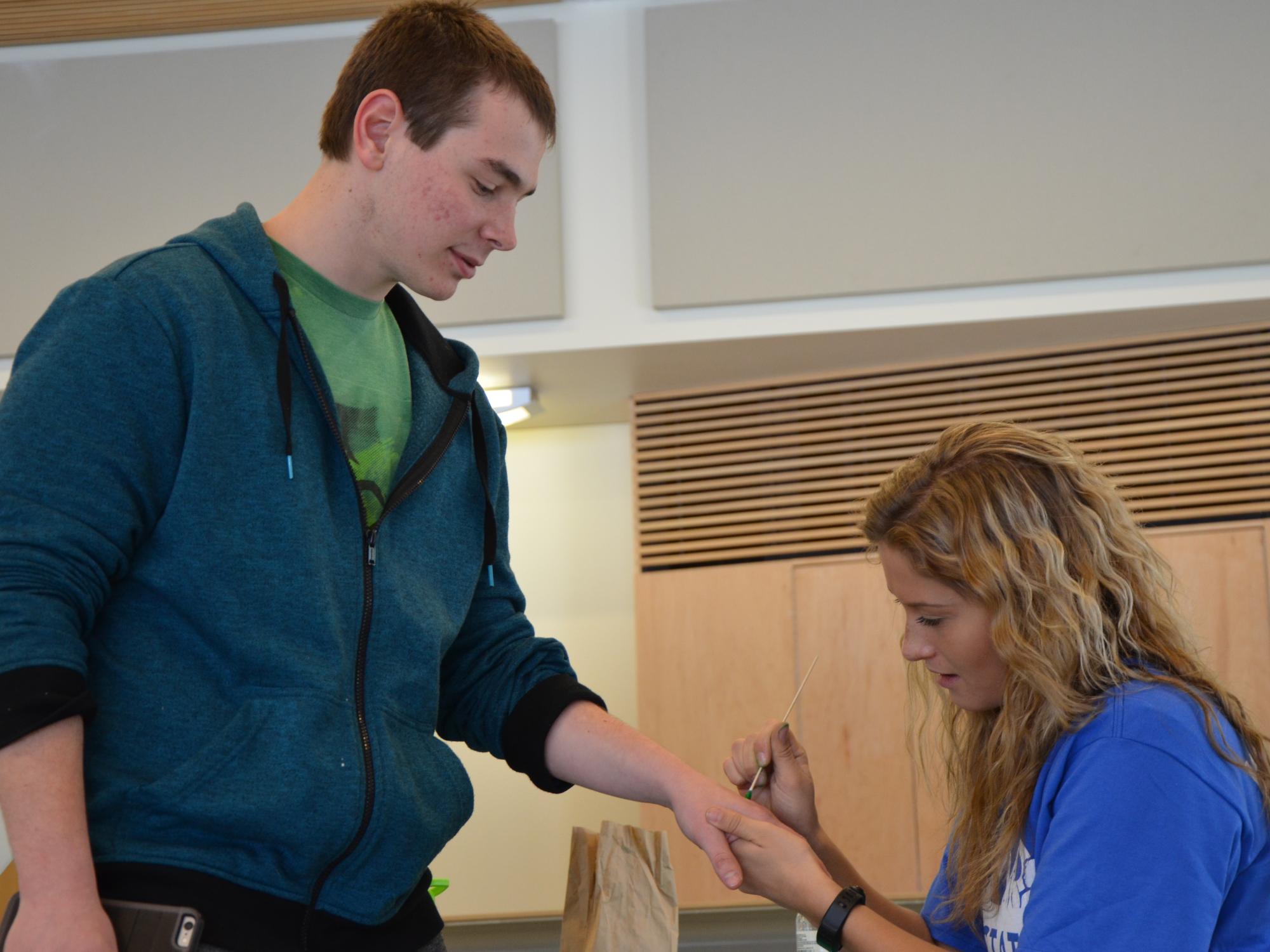 A student painting a green dot on another student's hand