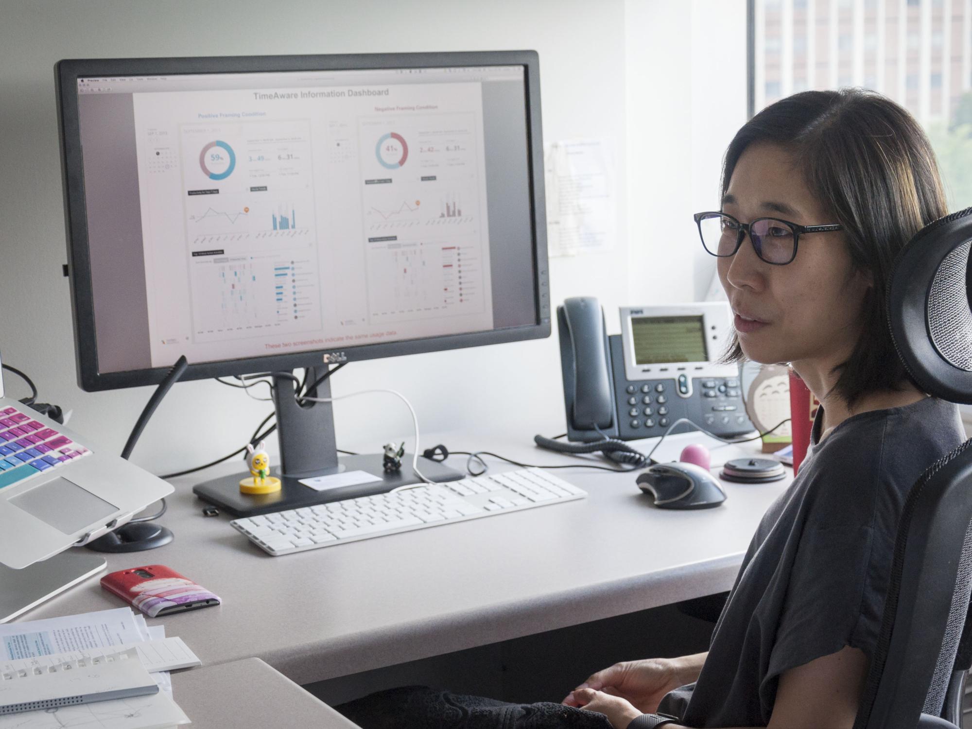 A woman sits in front of her desktop computer that is running the TimeAware web app 