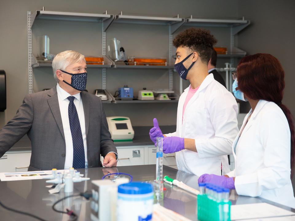 President barron looking at two students in lab coats.