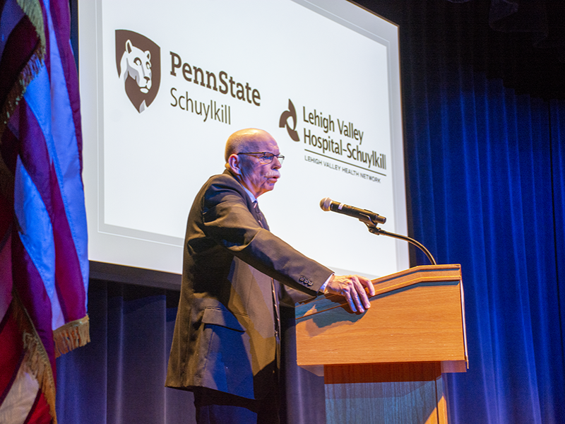 Bill Rowan delivers his presentation in front of a projected image of Penn State Schuylkill and Lehigh Valley Hospital - Schuylkill logos