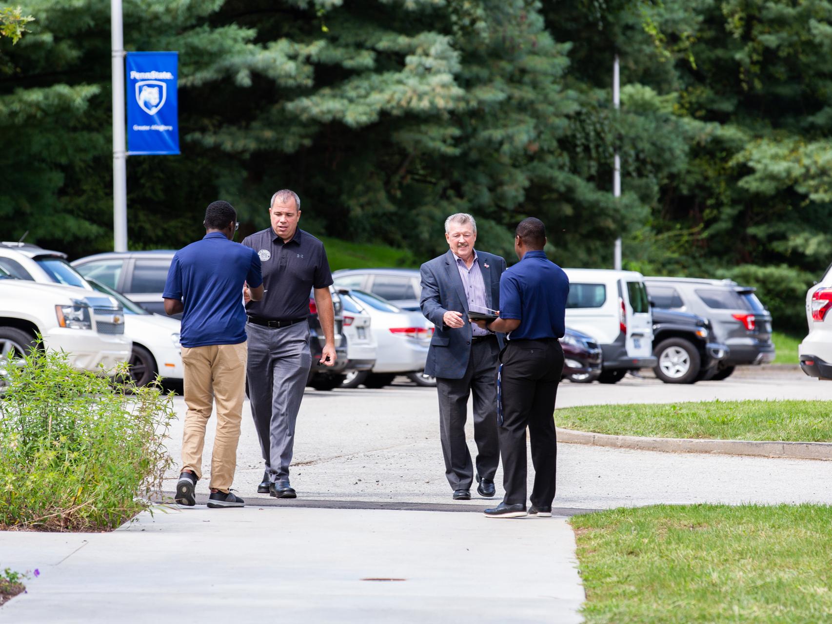 two men walking up to students receiving event programs. 