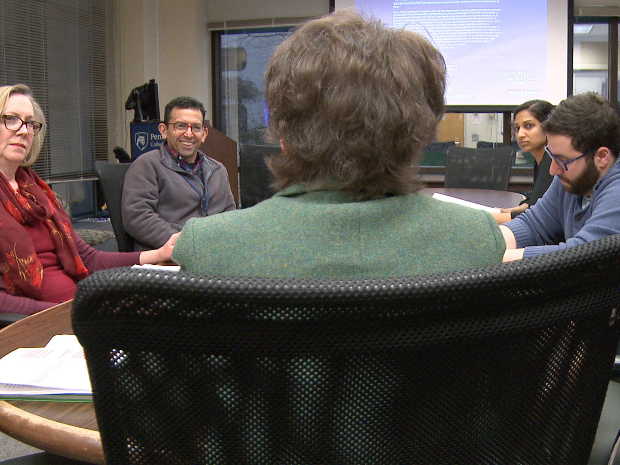 Dr. Eileen Moser, Dr. Jose Stoute, Dr. Nitasa Sahu and Dr. Samer Muallem sit around a wooden table in a conference room as Kimberly Myers, her back to the camera, begins a Writers Group workshop.