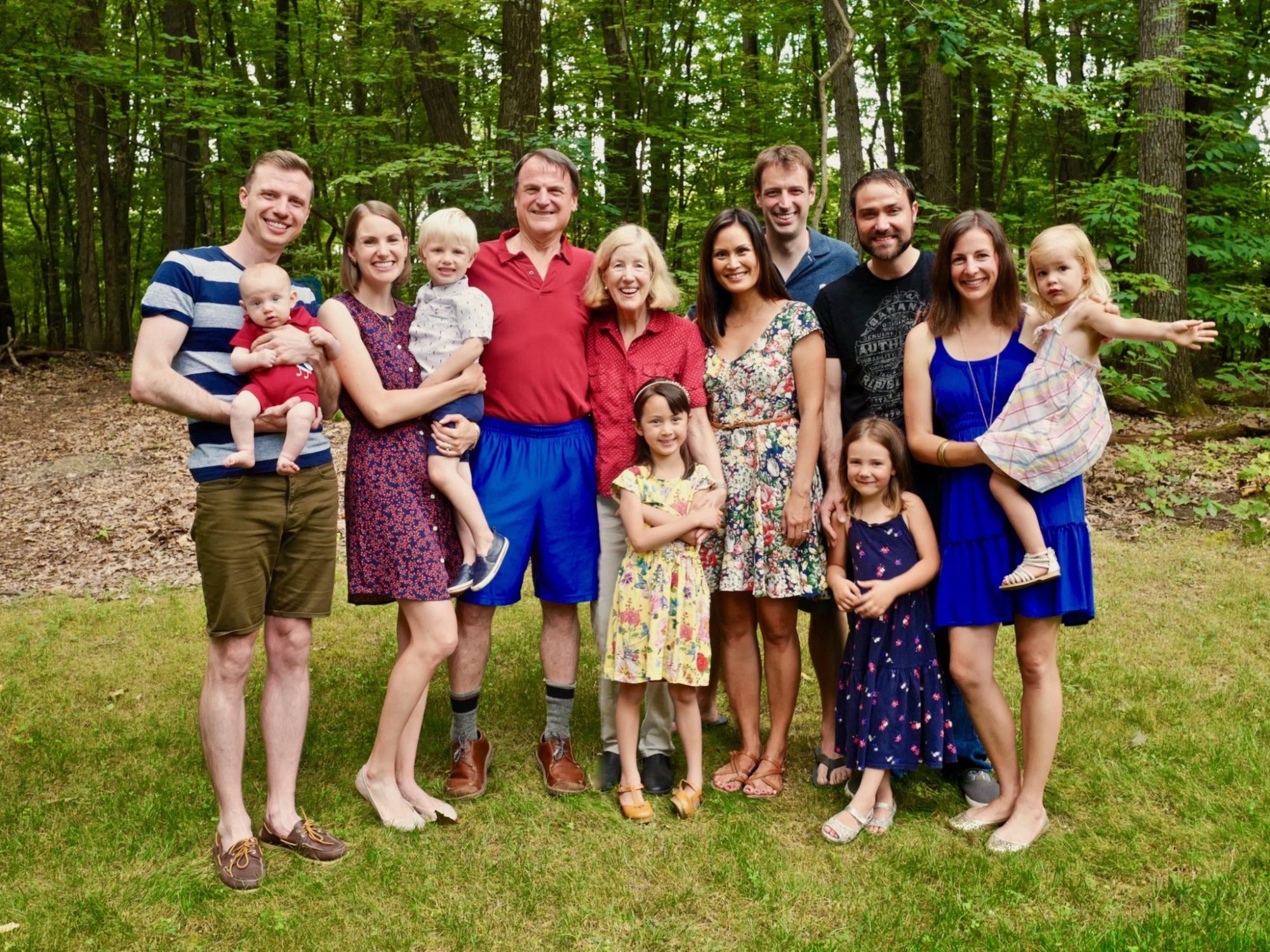 picture of a large family of all different ages smiling in front of wooded area