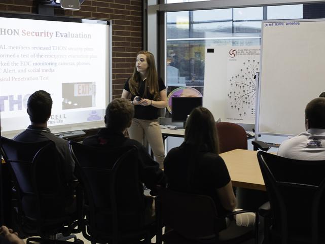 student looks at presentation screen while talking to a crowd of people in a conference room