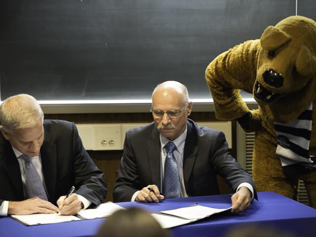 two men signing papers while the Nittany Lion watches