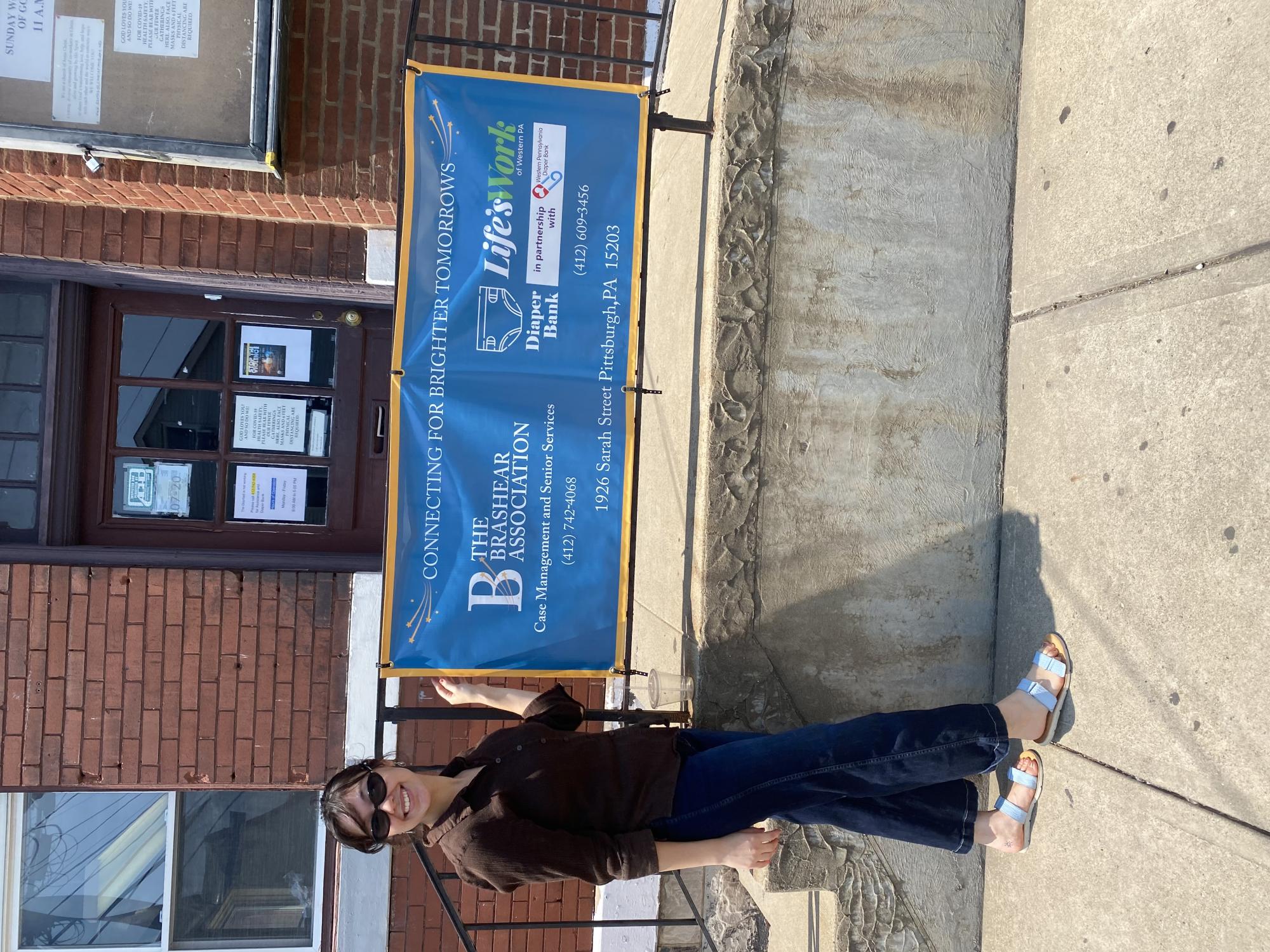 Student standing in front of a building pointing to a banner that reads Brashear Association.