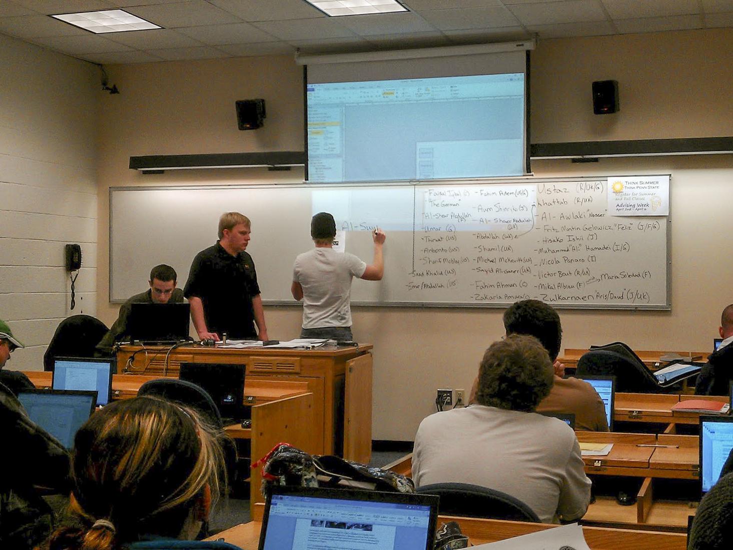 Students stand at a classroom whiteboard as other students watch