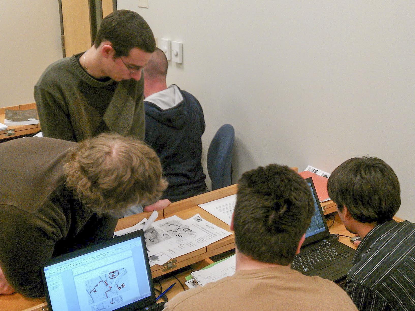 Students sit together while working at a computer on a desk