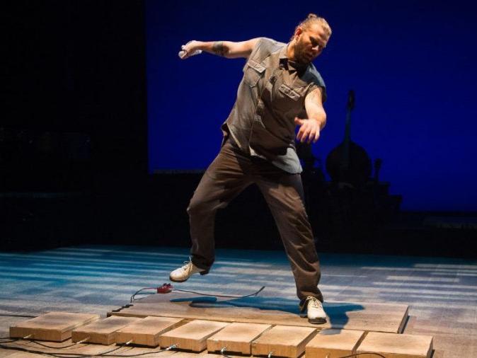 A dancer watches his feet as he taps on various percussive boards.