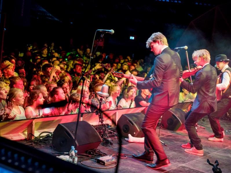 Three musicians stand on stage and play their instruments to an audience.