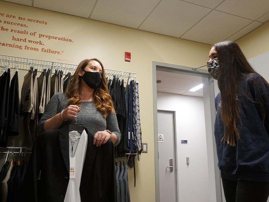 A student looks on as a staff member displays a professional outfit on a hanger.