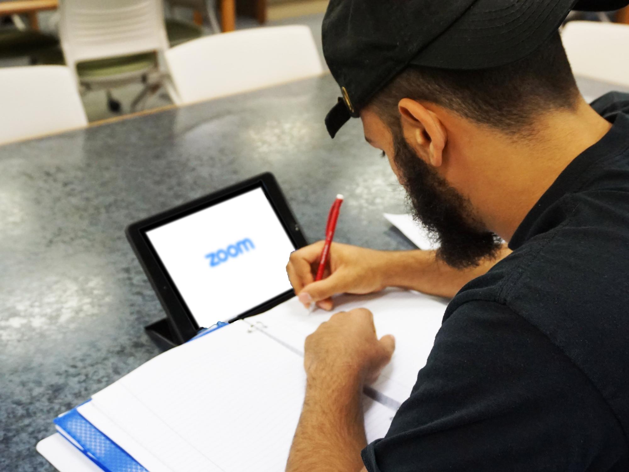 student writing notes and opening video conferencing software on iPad