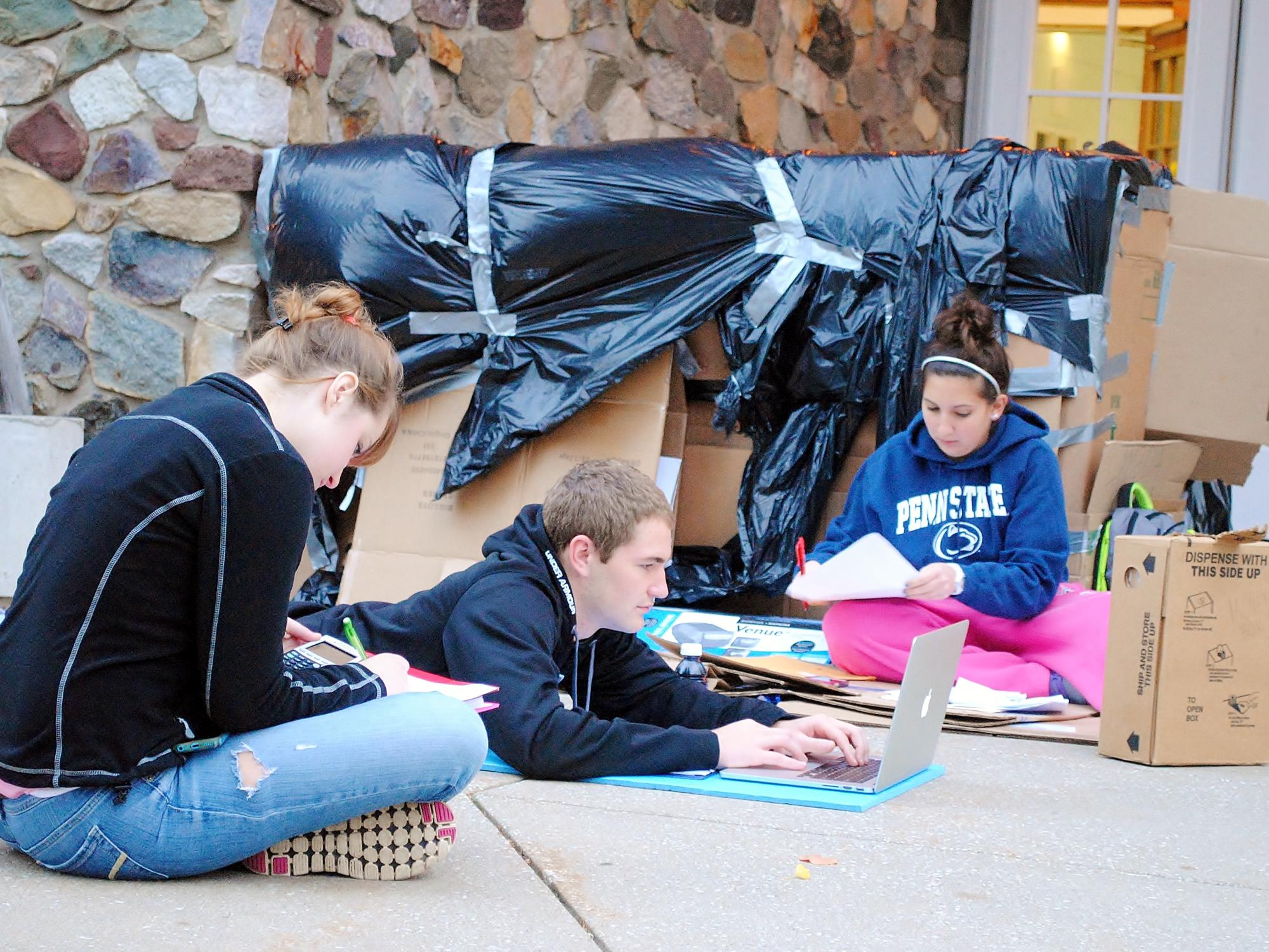 Students study outside a cardboard shelter.